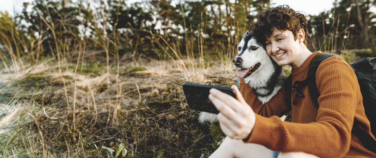 Junge Person macht ein Selfie von sich selbst und seinem Hund beim Wandern